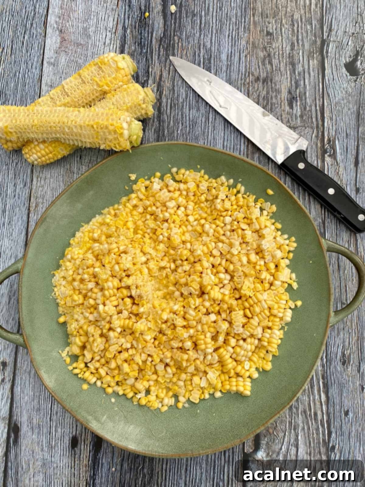 Fresh corn on a plate with corn cobs and a knife.