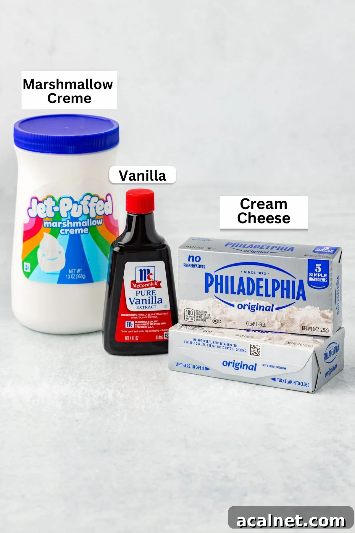 A jar of Jet-Puffed marshmallow creme, a bottle of vanilla extract, and a box of cream cheese arranged as classic ingredients for Marshmallow Fruit Dip.