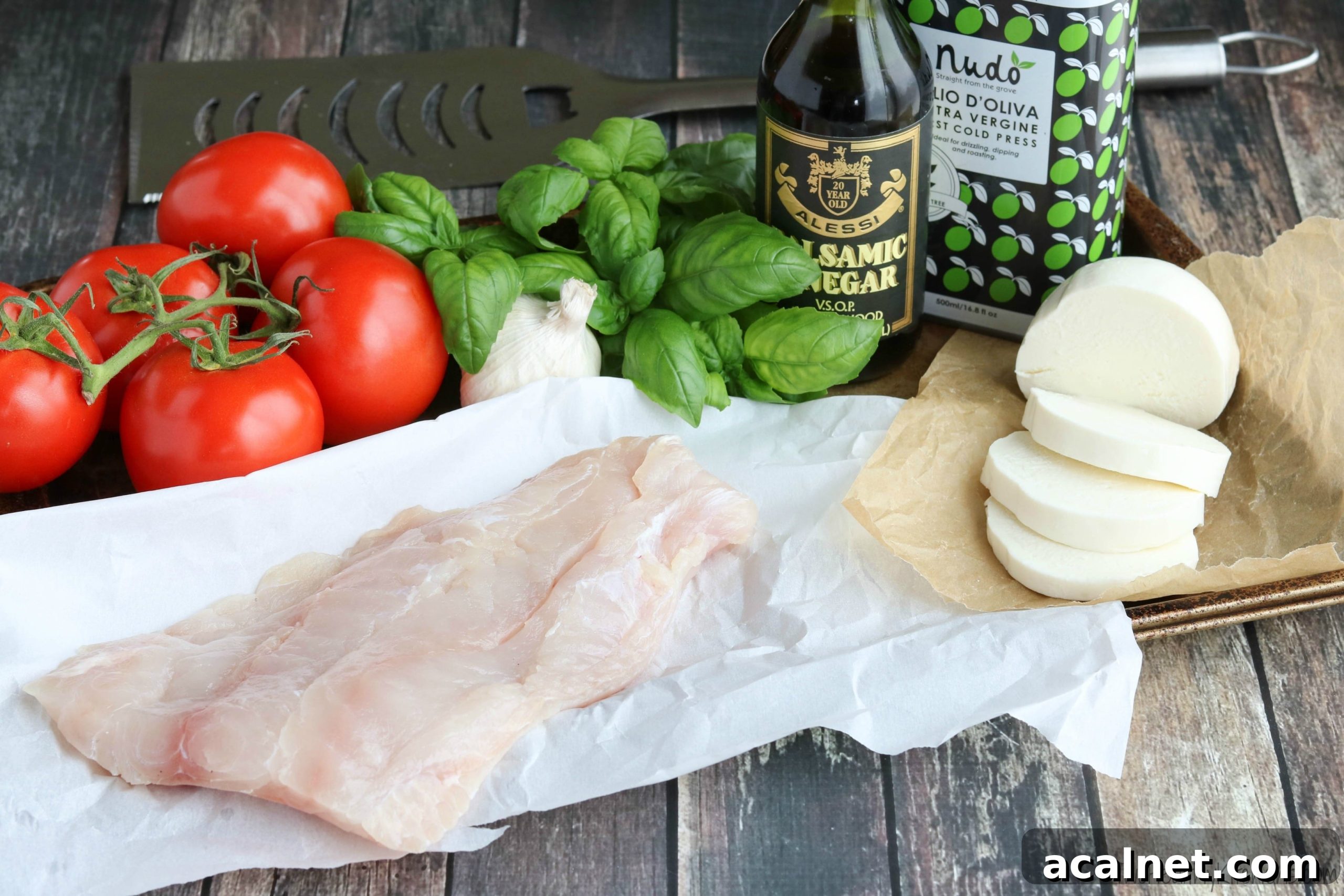 Caprese Grilled Fish Ingredients Watermarked Ingredients laid on wood background - raw fish filet, vinegar and oil, and fresh garlic, tomatoes, basil and mozzarella.