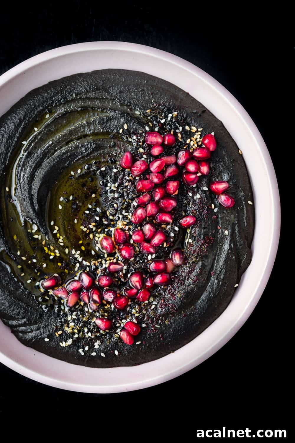 black hummus in a pink bowl with toppings, overhead shot