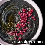 black hummus in a pink bowl with toppings, overhead shot