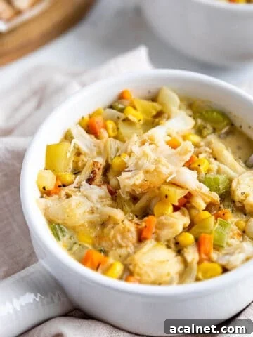 A soup bowl with a handle filled with a crab and corn chowder.