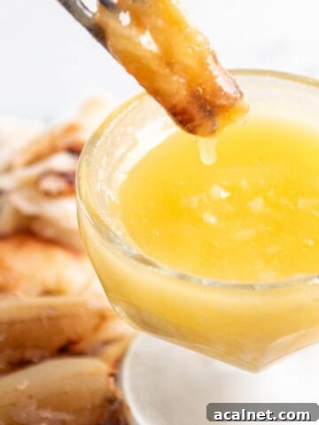 A piece of crab meat being dunked into a bowl of butter.