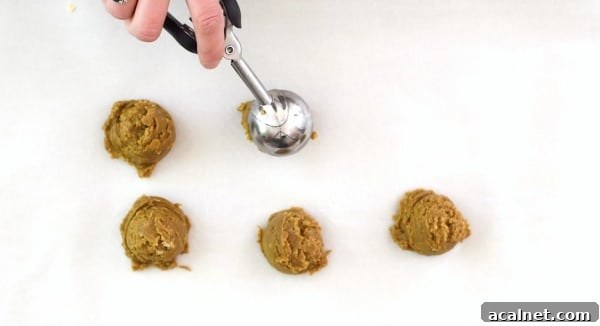 A cookie scoop dropping cookie dough balls onto a baking sheet.