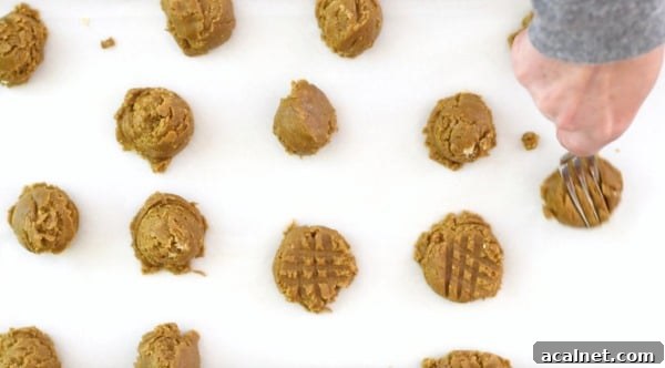 A fork pressing the cookie dough down to be flatter.