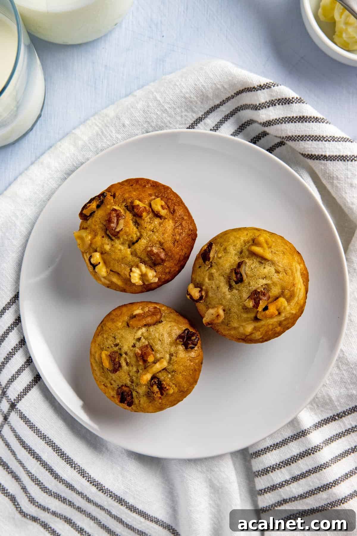 Moist Banana Walnut Muffins with Crumbly Streusel Topping 2 Three baked muffins on a white plate with a glass of cold milk in the background.