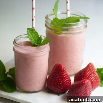 Dairy-Free Strawberry Milkshake Recipe: Creamy Vegan Shake 7 Two strawberry dairy-free milkshakes with straws and sprigs of mint on a tray with fresh strawberries.
