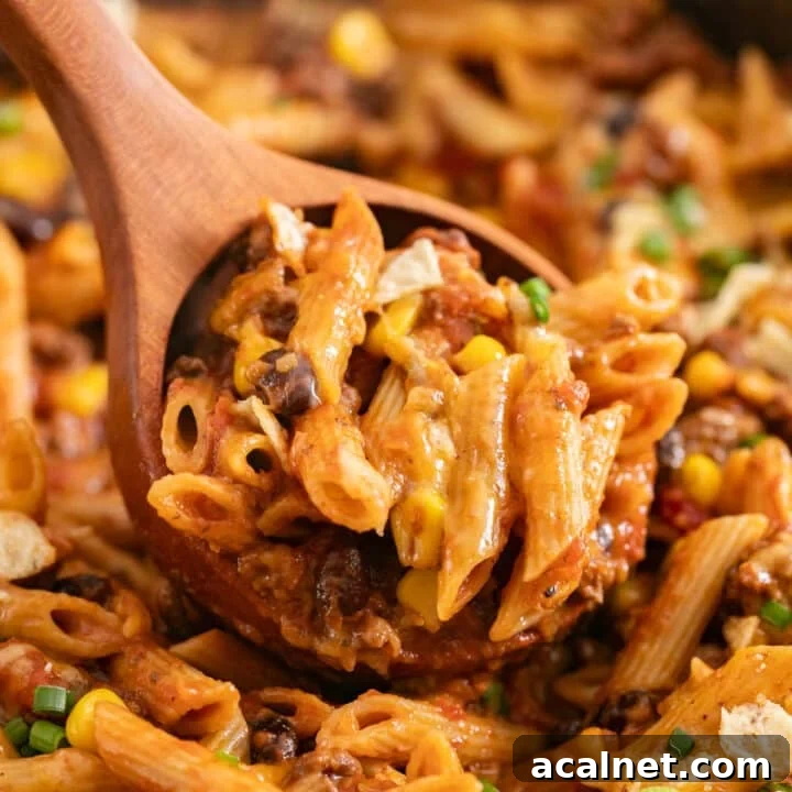 A wooden spoon scooping up creamy taco pasta from the pan.