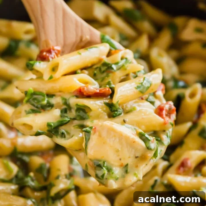 A wooden spoon holding a scoop of creamy chicken Florentine pasta over the full pan of it.