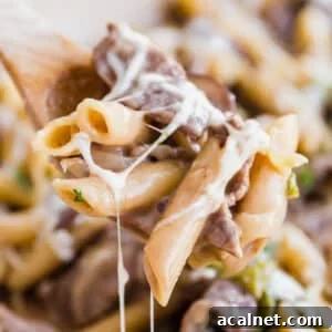 A wooden spoon holing a scoop of Philly steaks pasta with melty cheese all over it.