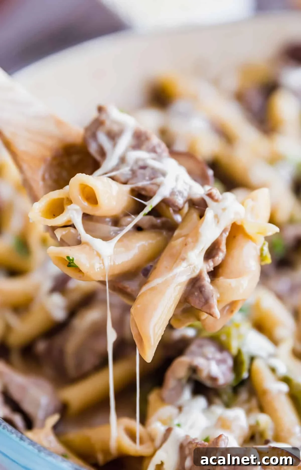 A wooden spoon holing a scoop of Philly steaks pasta with melty cheese all over it.