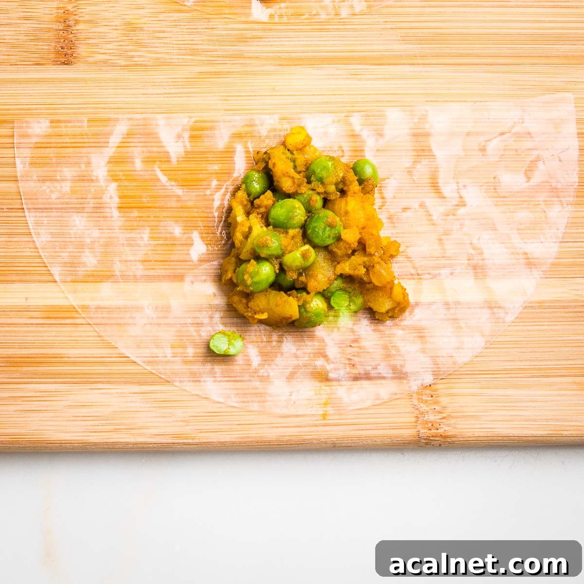 Half moon of moistened rice paper on a wooden board with a scoop of potato samosa filling