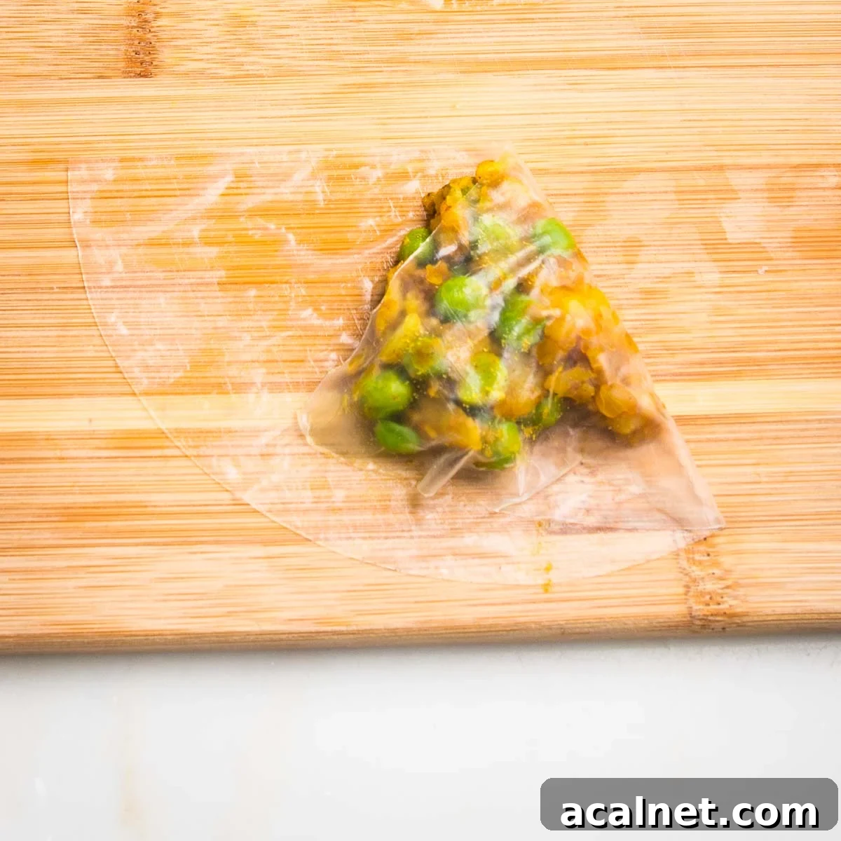Half moon of wet rice paper, with a scoop of potato samosa filling, with one side folded over.