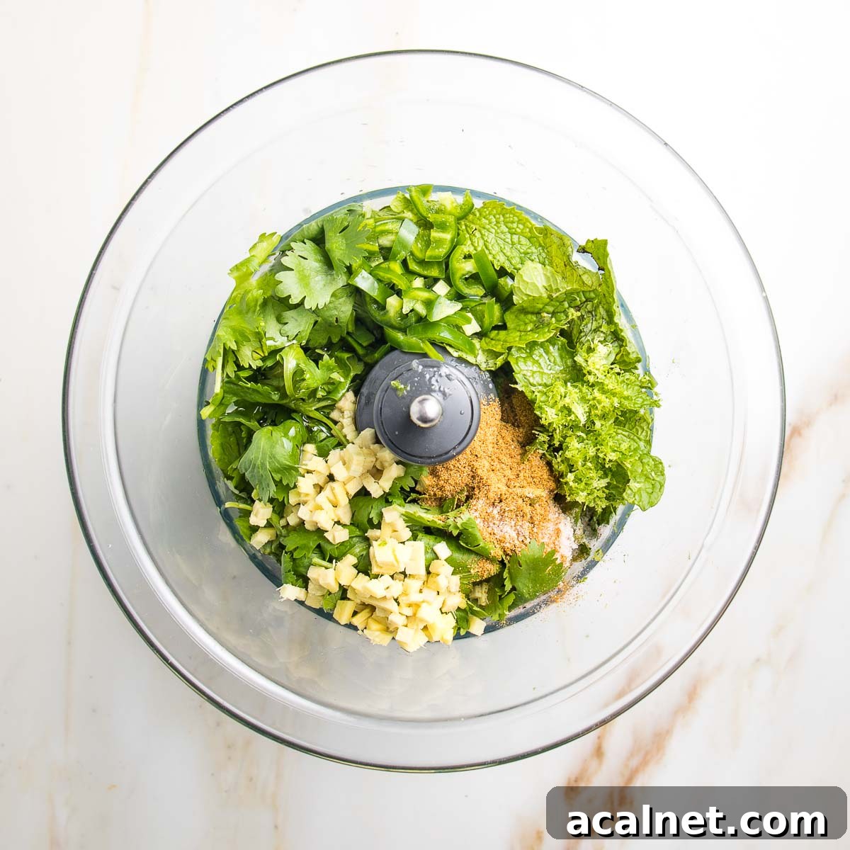 Food processor bowl with fresh cilantro and mint, minced ginger, jalapeno, honey, spices.
