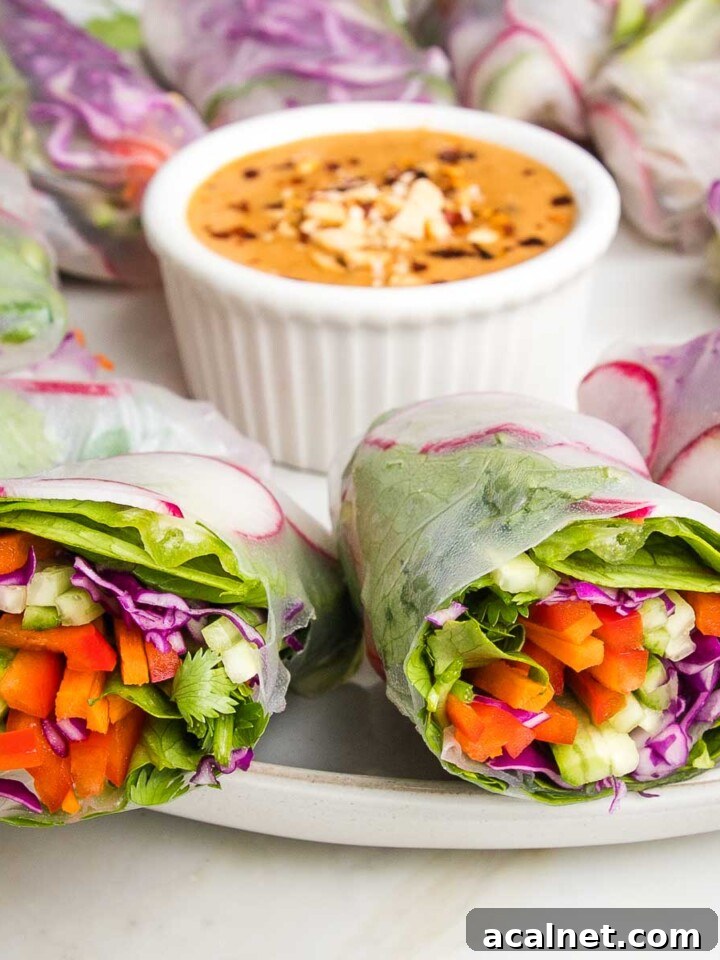 Fresh spring rolls cut in half with colorful julienned veggies shown and a small dish of peanut sauce. veggies