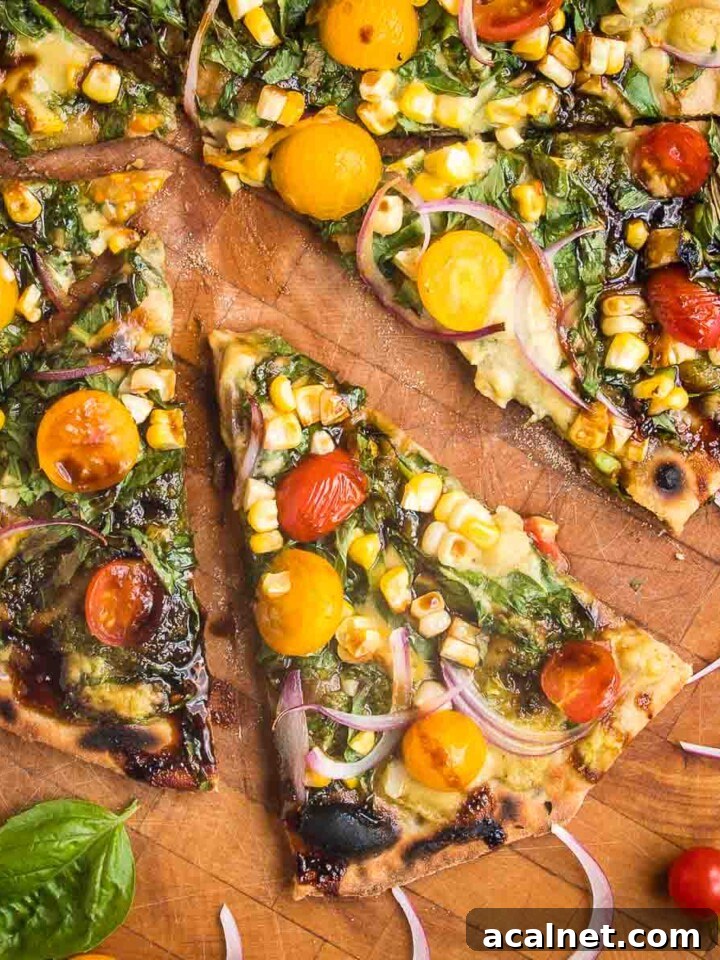 Flatbread Pizza with pesto, hummus, yellow and red tomatoes plus fresh basil and red onions. One slice shown up close and a few others partially shown on a wooden cutting board.