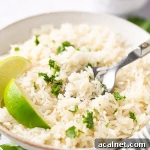 instant pot coconut rice topped with cilantro and a wedge of lime in a white bowl with a silver spoon