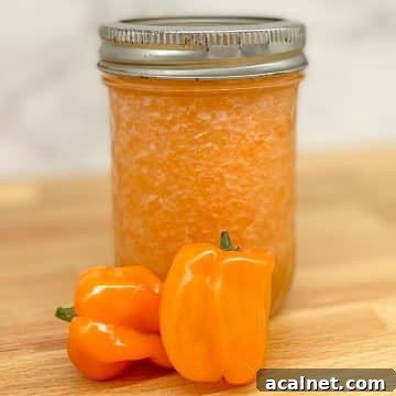 Pineapple habanero sauce in a glass jar with two habaneros on a butcher block counter.