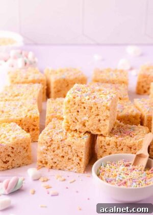 A stack of rice krispie treats on a pale purple background with a small bowl of pastel sprinkles, text overlay reads "gluten free rice krispie treats."
