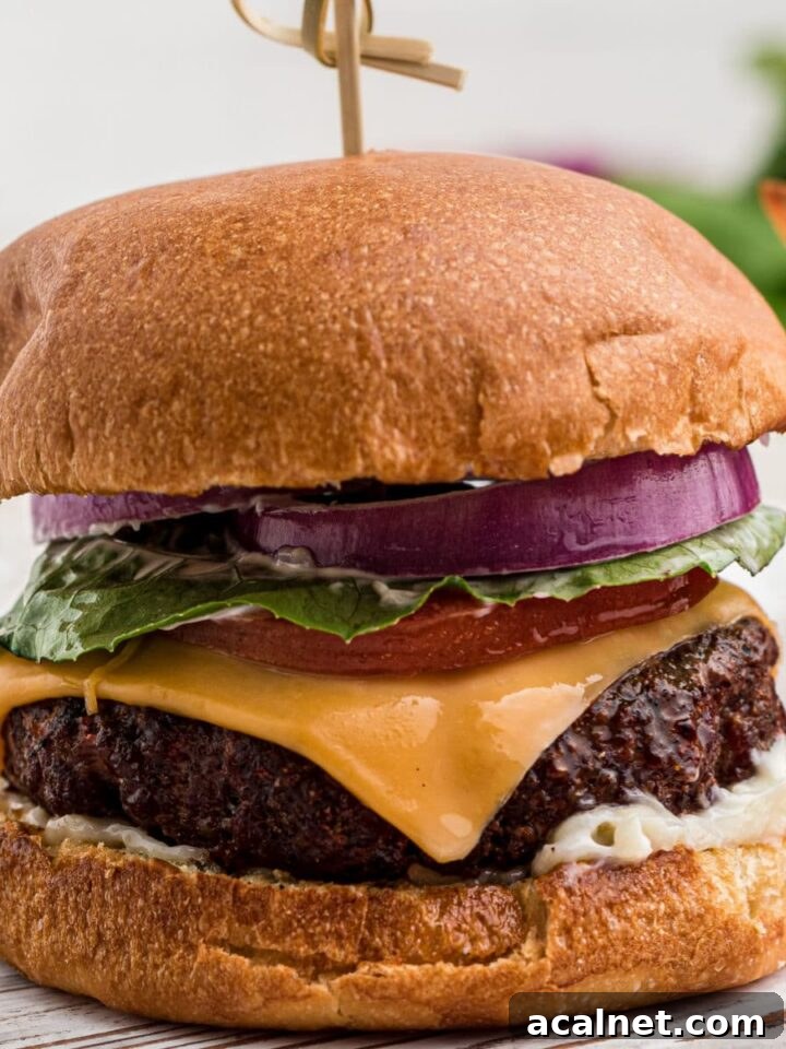 close up of a dressed venison burger with a bowl of french fries in the background