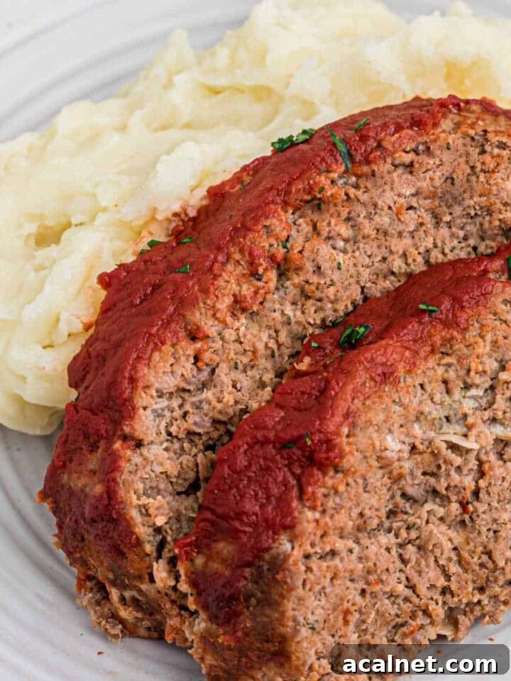 Close up shot of two slices of venison meatloaf against some mashed potatoes.