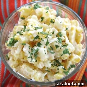 Mexican Street Corn Cups Recipe – Creamy Elote in a Cup 12 Mexican street corn in a glass cup topped with Cotija cheese and chopped cilantro on a colorful napkin.