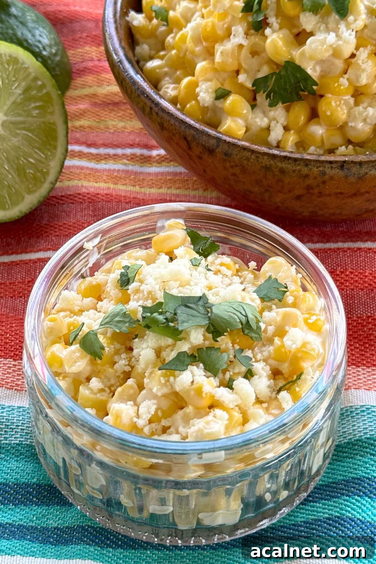 Mexican Street Corn Cups Recipe – Creamy Elote in a Cup 8 Mexican street corn in a glass cup with a lime and a bowl with more street corn behind it.