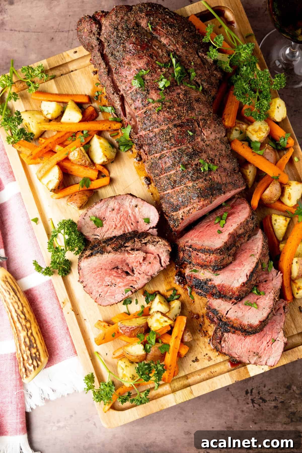 Smoked beef tenderloin on wood cutting board sliced to serve with potatoes and carrots surrounding the meat.
