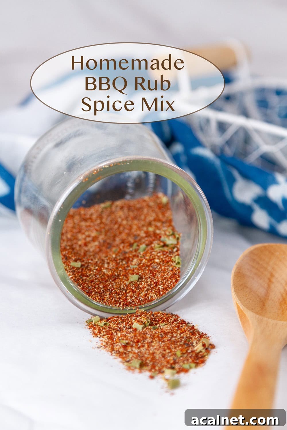 spice mix in a glass jar that's tipped over so the spice spilled out with a wooden spoon and a blue cloth.