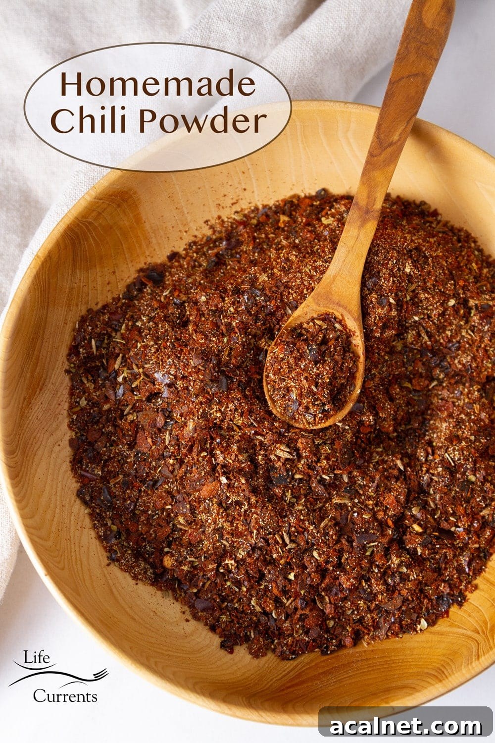 a wooden bowl filled with chili powder spice and a wooden spoon in the spice.