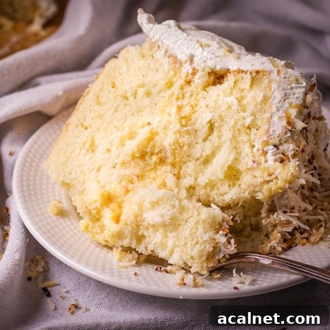 A slice of coconut cream cake on a plate with a fork, ready to eat.