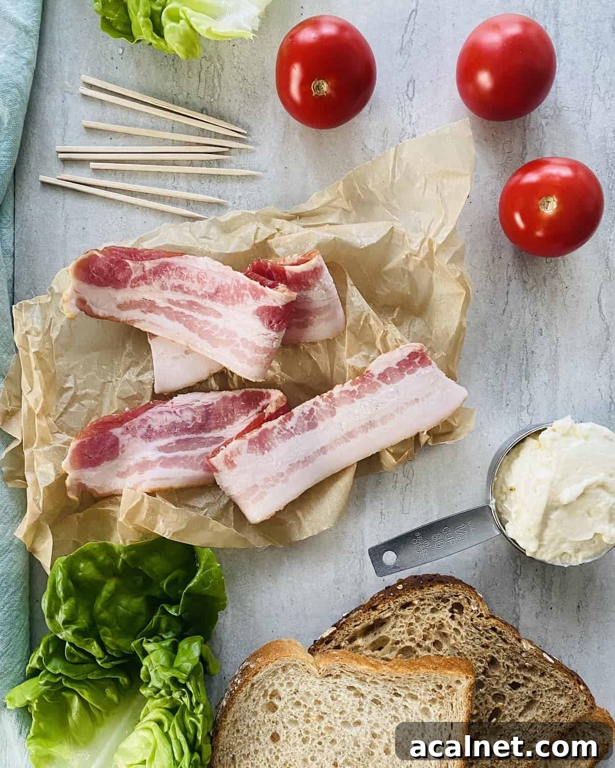 Bacon, tomatoes, lettuce, mayonnaise and slices of bread on a marble board.