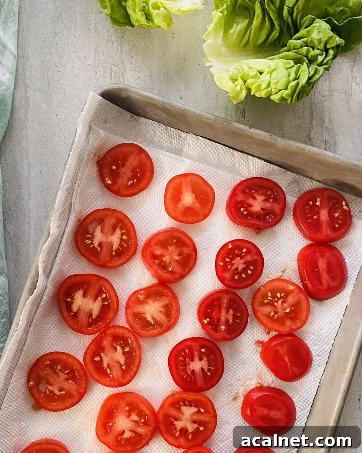 Slices of tomatoes draining on a paper towel lined baking sheet.