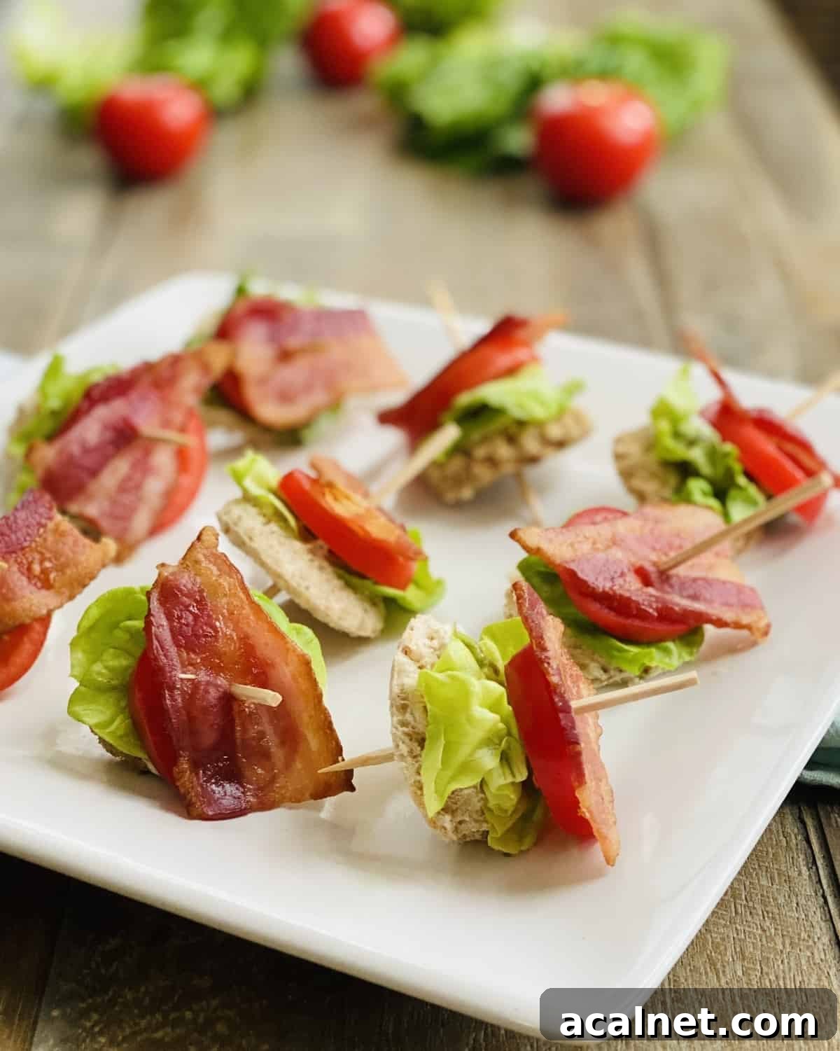 A white platter with bacon, lettuce and tomato appetizers.