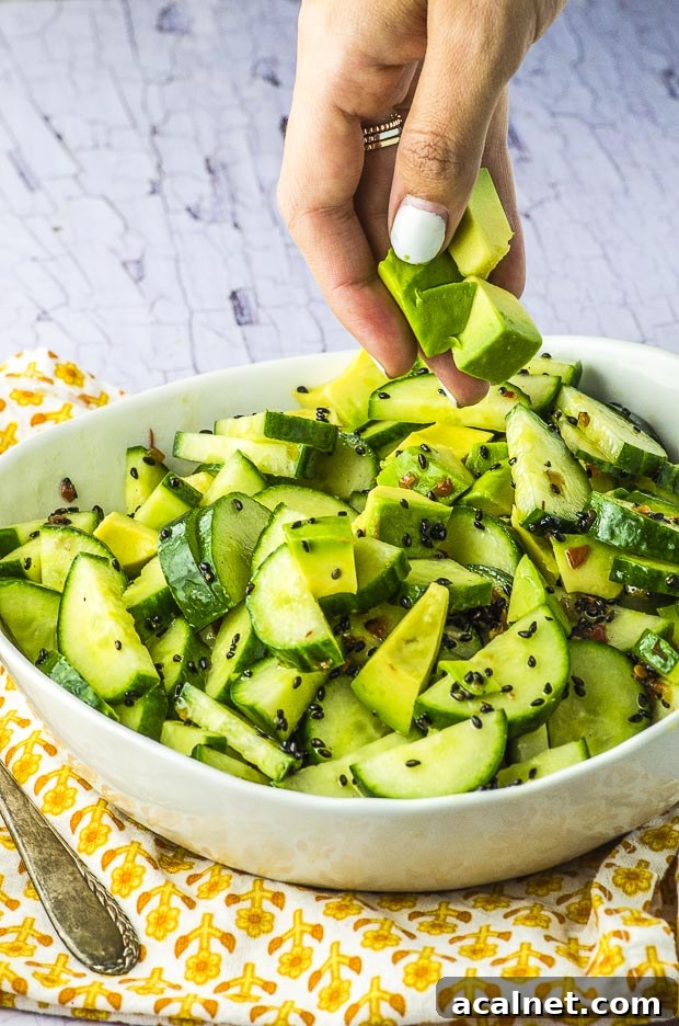 Avocado cucumber salad in a white bowl, with some diced avocado being added to the bowl
