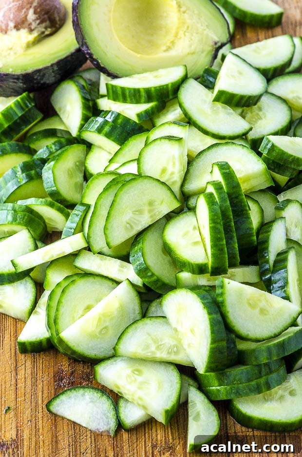 Cucumber slices and an avocado cut in half on a wooden cutting board