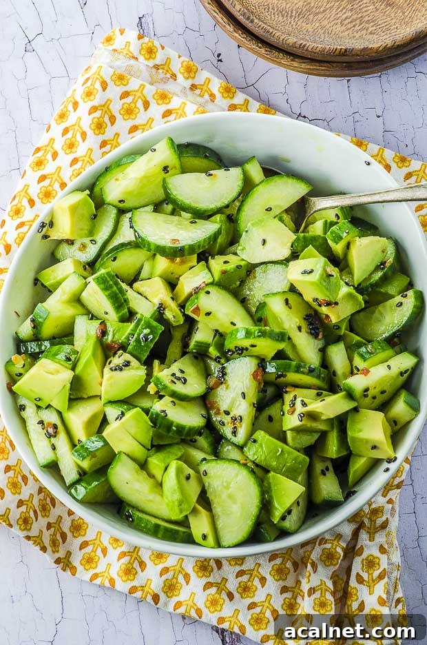 Birds eye view of the avocado cucumber salad in a white bowl, over a white and yellow cloth napkin