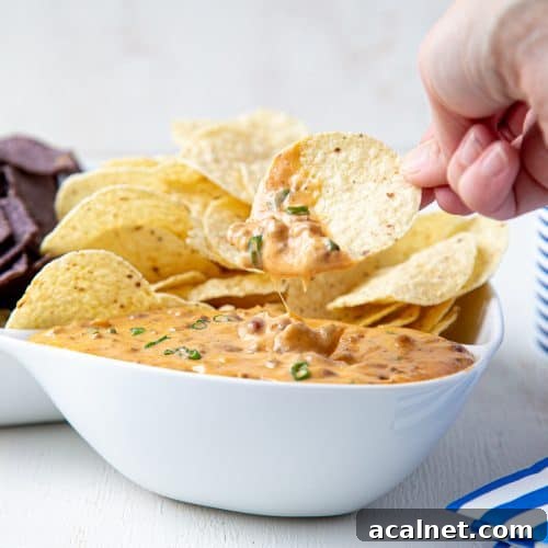 hand dipping a chip into nacho cheese dip in a white bowl.