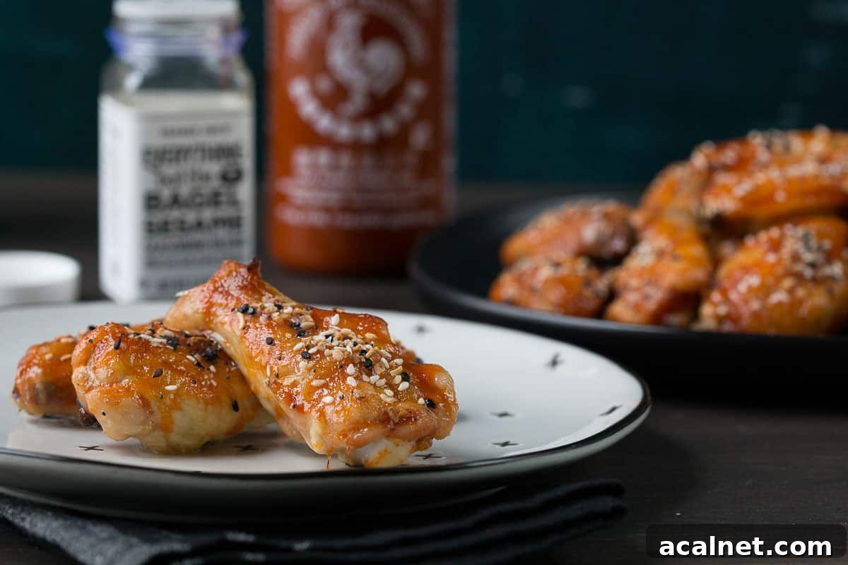 baked chicken wings on a white plate next to a bottle of sriracha and a jar of everything bagel seasoning.