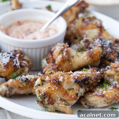 Grilled chicken wings on a white platter with a small bowl of sun dried tomato mayo