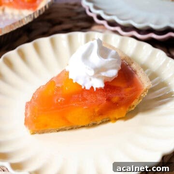Peach jello pie with peach chunks set in peach gelatin in a graham cracker pie crust topped with whipped topping.