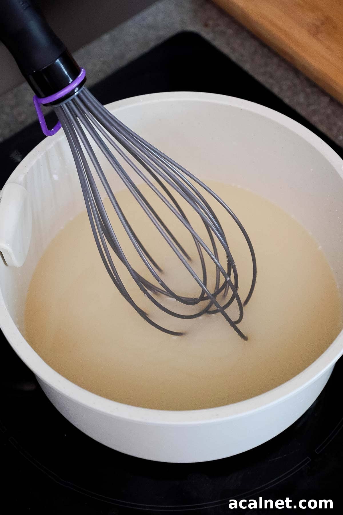 A saucepan with a whisk stirring water, sugar, and cornstarch.