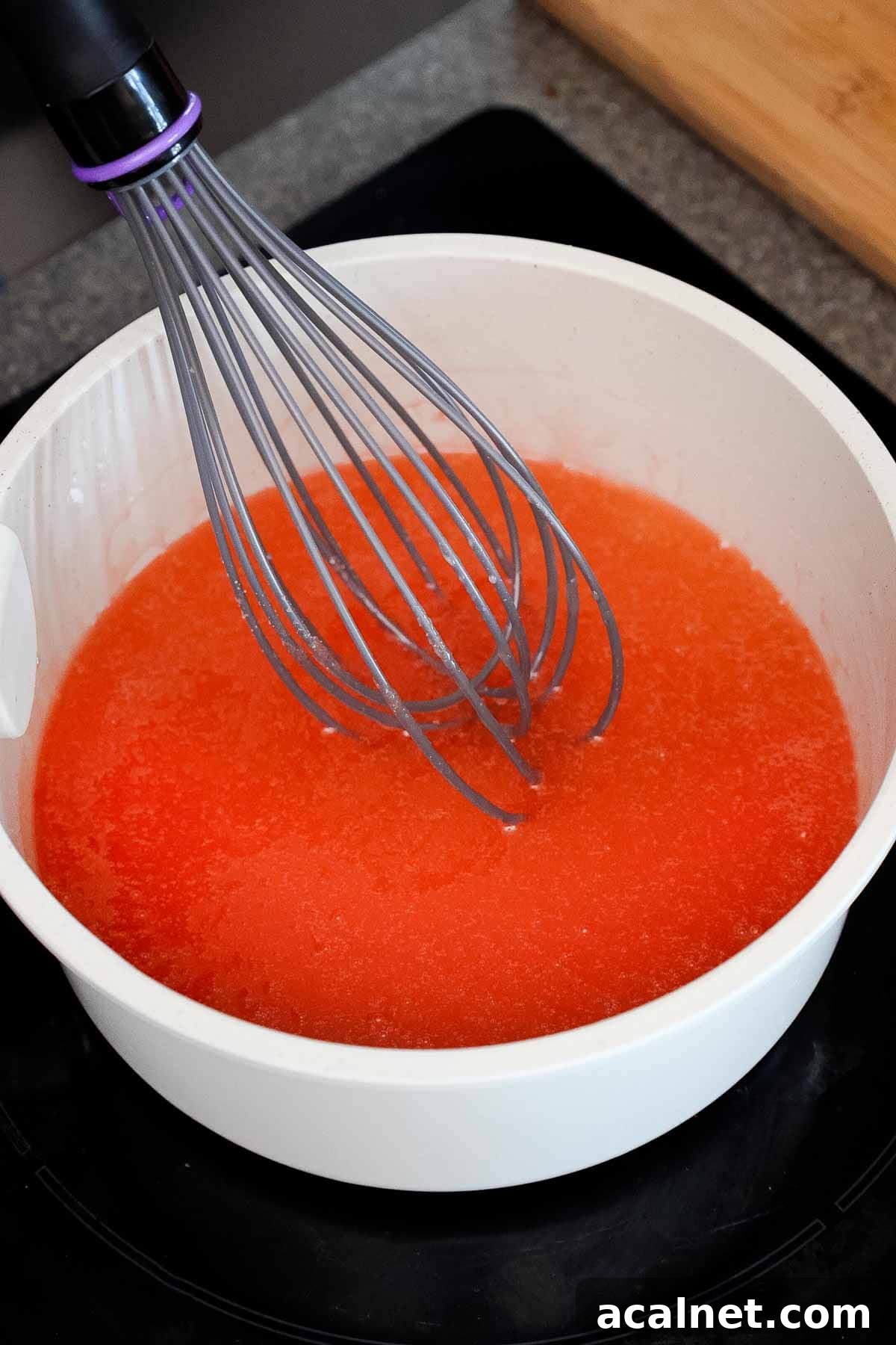A saucepan with a whisk in a peach gelatin mixture.