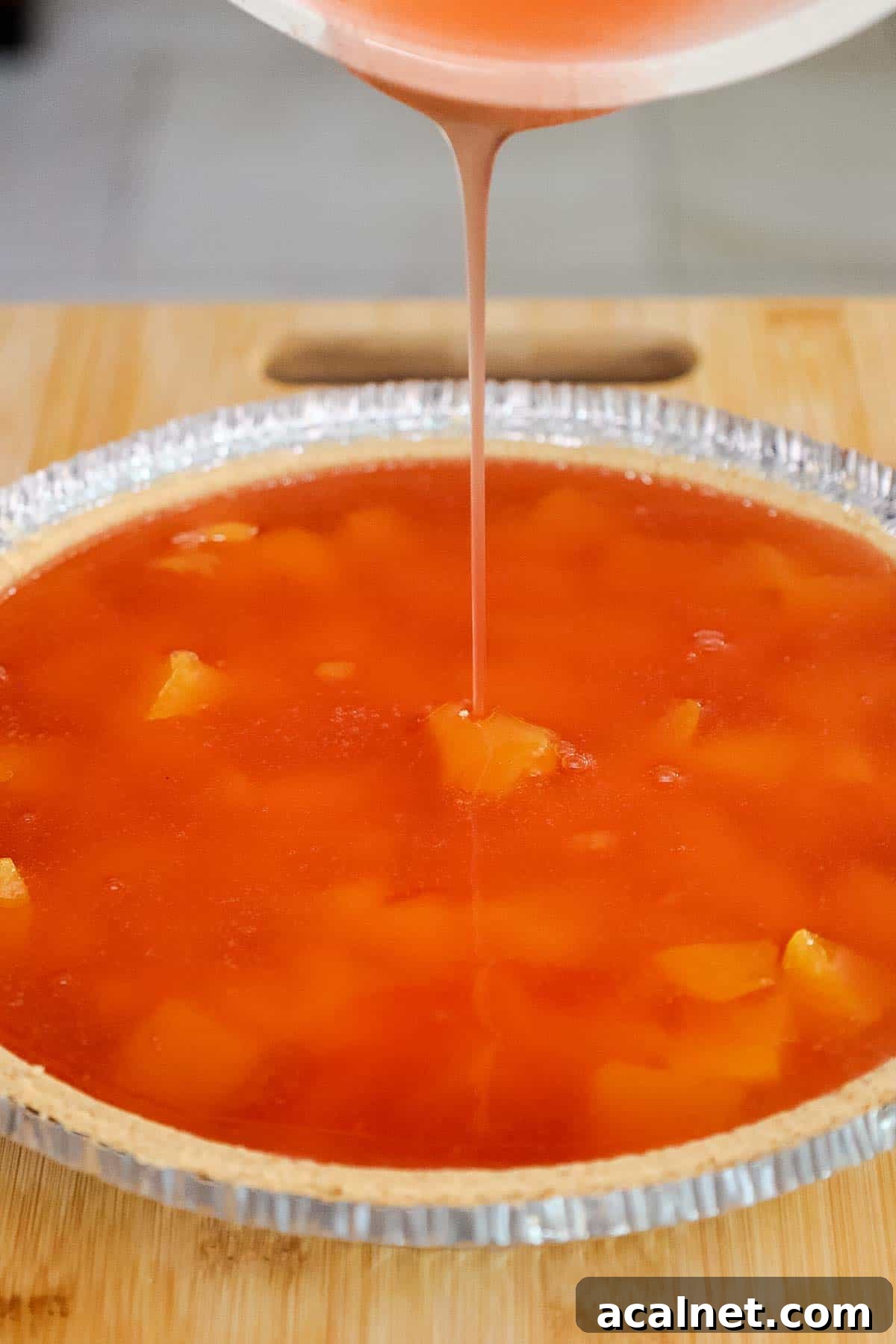 Peach gelatin mixture being poured over peaches in a pie crust.