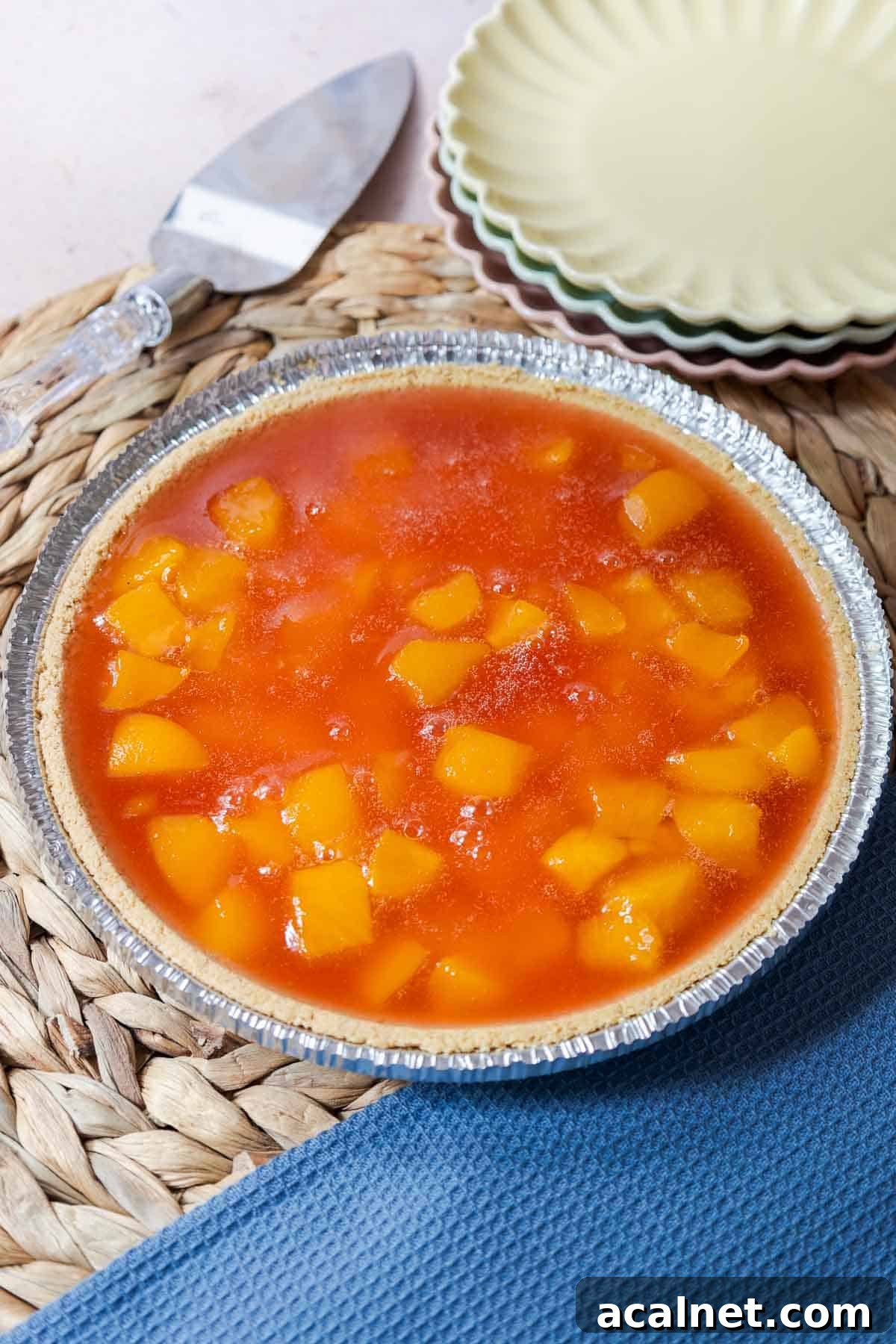A finished peach Jello pie with peach chunks set in peach gelatin in a graham cracker pie crust.