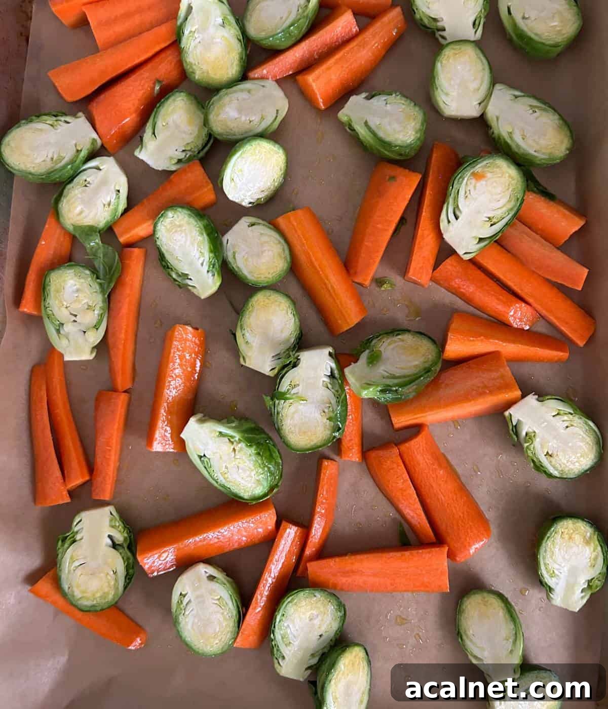 Carrots and brussels sprouts on cookie sheet lined with parchment paper.