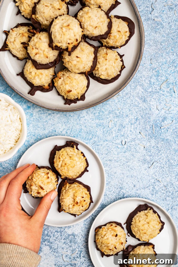 Coconut macaroons on a few plates on a light blue background, a hand is reaching for one of the cookies.