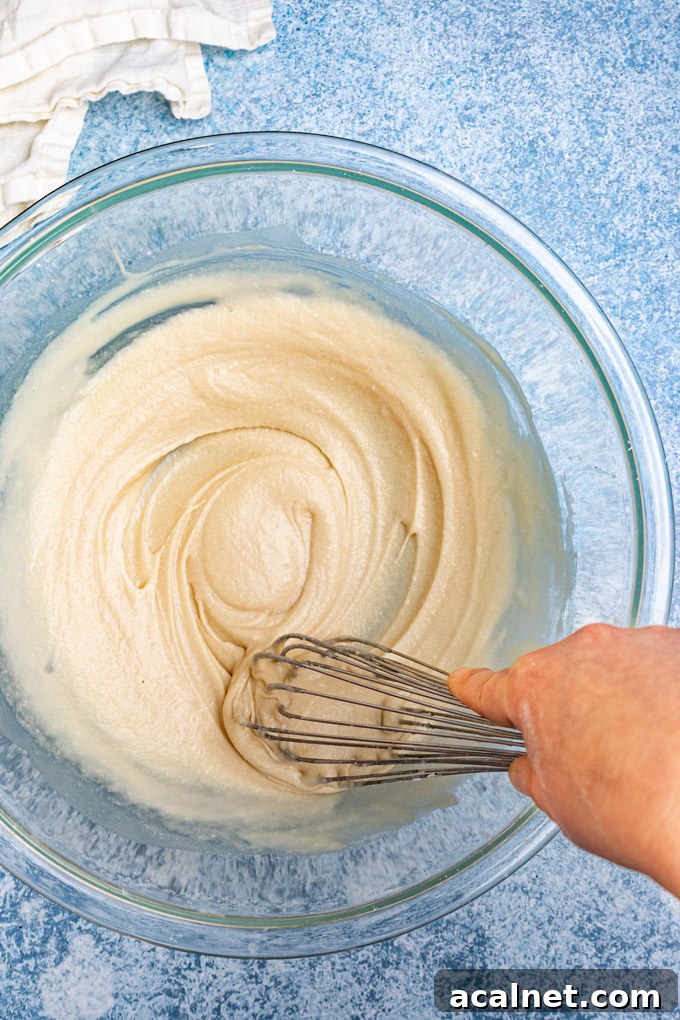 Coconut cream, and honey being whisked together in a large mixing bowl.