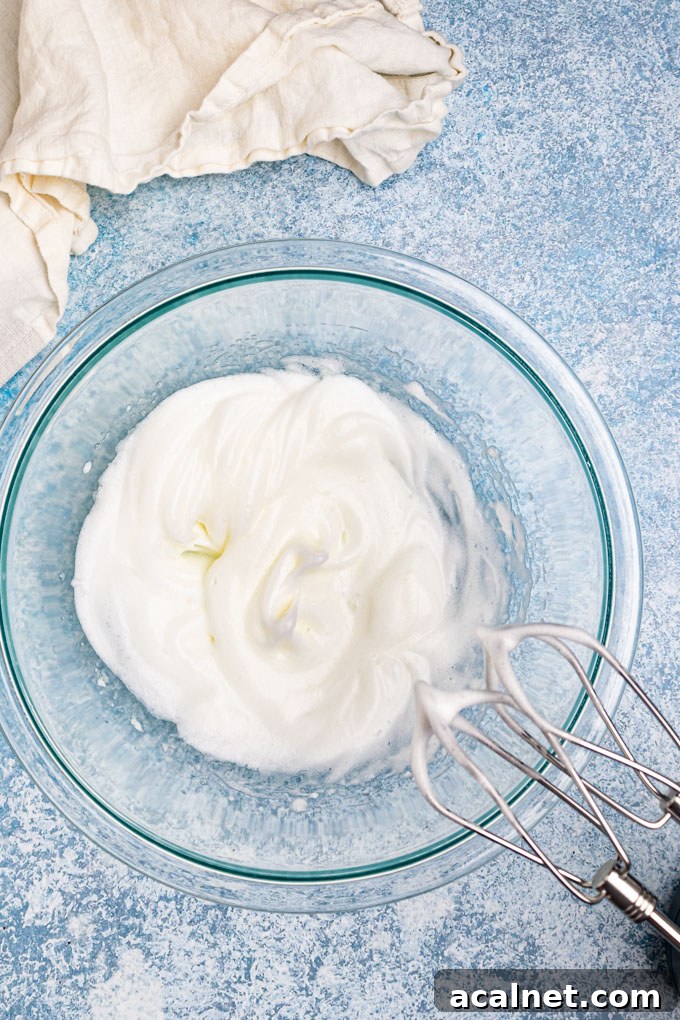 Egg whites in a bowl whisked up into stiff peeks with a hand mixer off to the side.