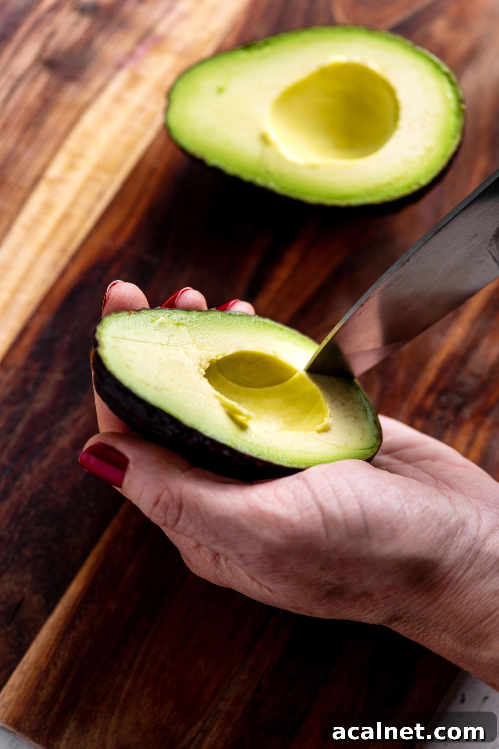 Woman cutting avocado in the shell with a knife.